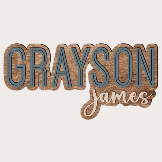 Custom wooden double name sign with the names 'Grayson' and 'James' displayed in a stylized font with a dark stain on the wood.