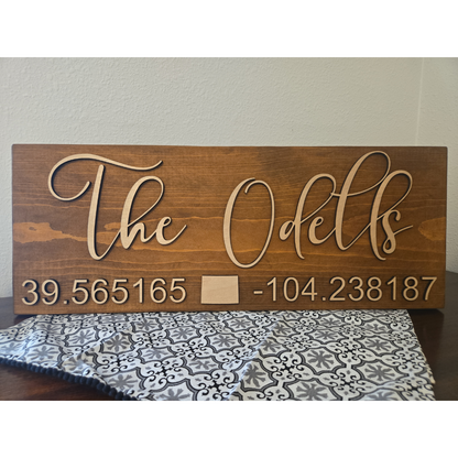 A wooden plank sign with the text 'THE ODELLS' laser cut on top, followed by a set of coordinates.